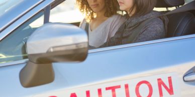 Two women sitting in a car with a caution sign.