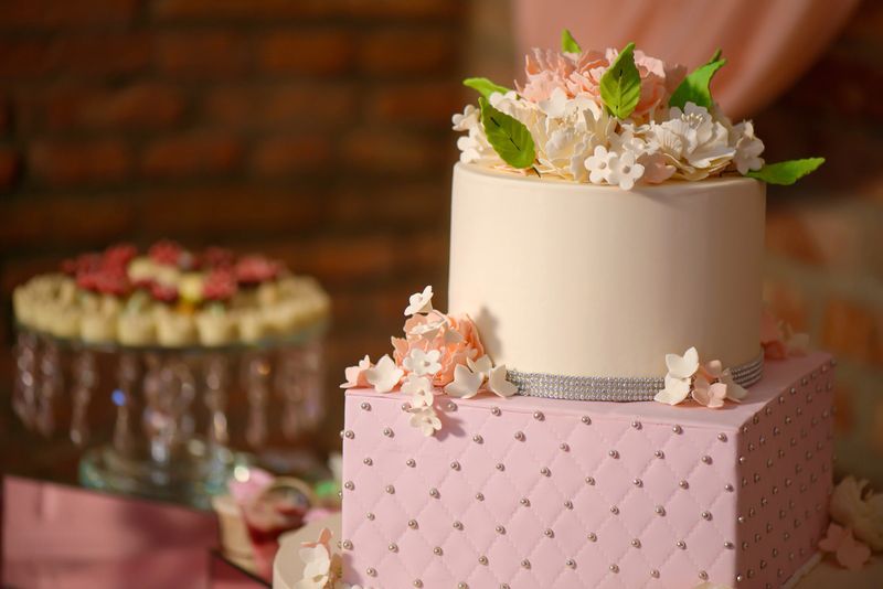 Horizontal shot of assortment of bite-sized cakes and a large three tiered cake embellished with velvet icing and sugar flowers, delicious dessert display at a wedding reception, a birthday party or a formal event.