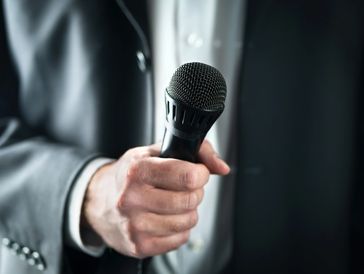 Close-up of a person holding a microphone in a suit.