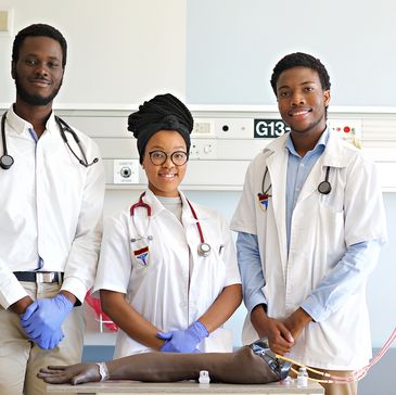 Three medical professionals in a clinical setting with a training arm model.