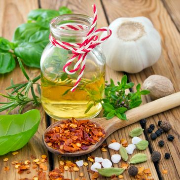 A jar of oil with herbs and spices on a wooden table.