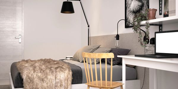 Cozy bedroom with a bed, wooden chair, and desk with laptop.