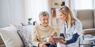 Nurse explains medication to elderly woman at home.