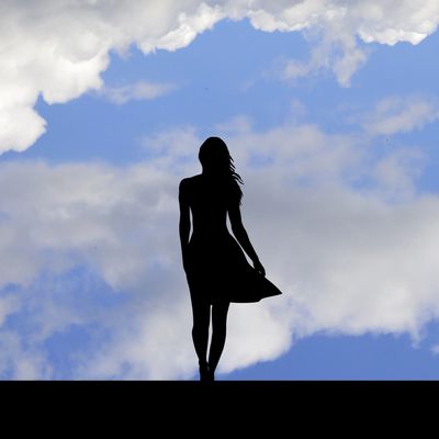 Silhouette of a woman against a partly cloudy blue sky.