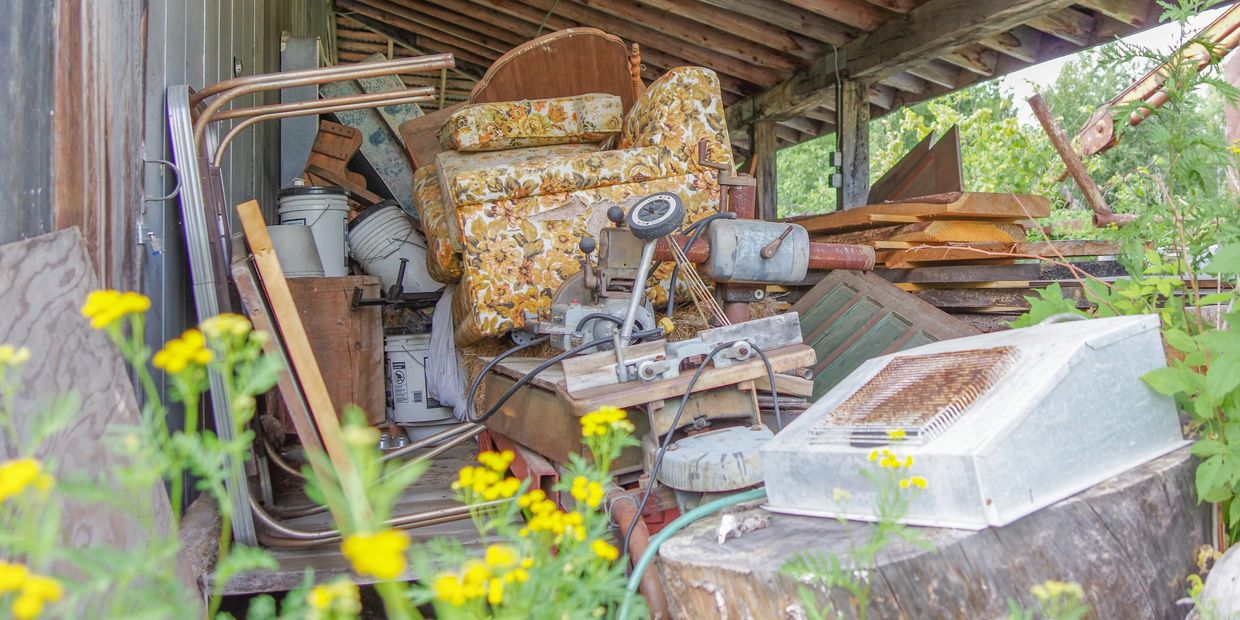 Pile of junk in backyard under patio with yellow flowers in front