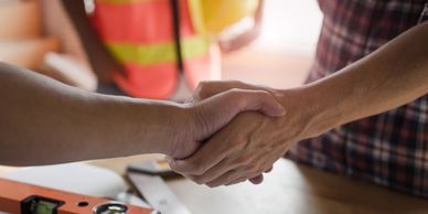 Two people shaking hands over a work table with construction tools.