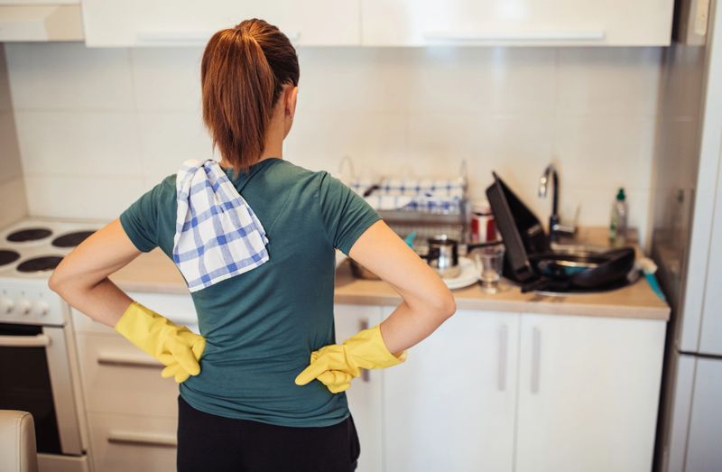 Young housewife is standing in the kitchen, wearing protective gloves, ready from washing dishes.