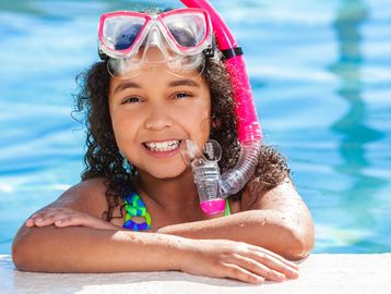 Smiling girl with snorkeling gear in a pool on a sunny day.