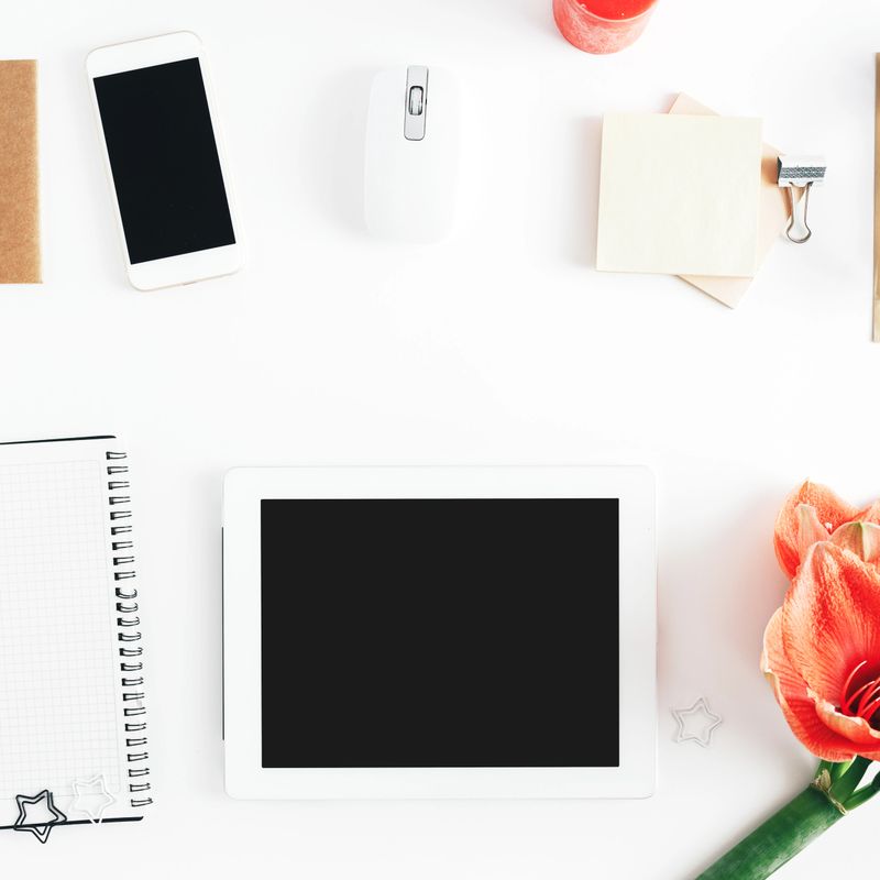 Flat lay home office desk table. Feminine workspace with tablet with copy space, notebook, smartphone, flowers and personal accessories top view