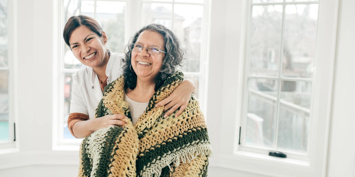 Two women smiling, one wrapped in a knitted blanket.