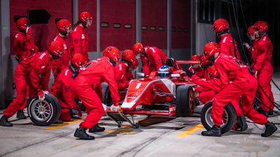 Race car pit stop with crew in red uniforms.