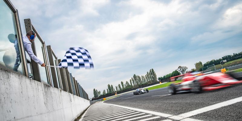 Blurred red formula race car about to win the race as a man on the left is waving a checkered flag.