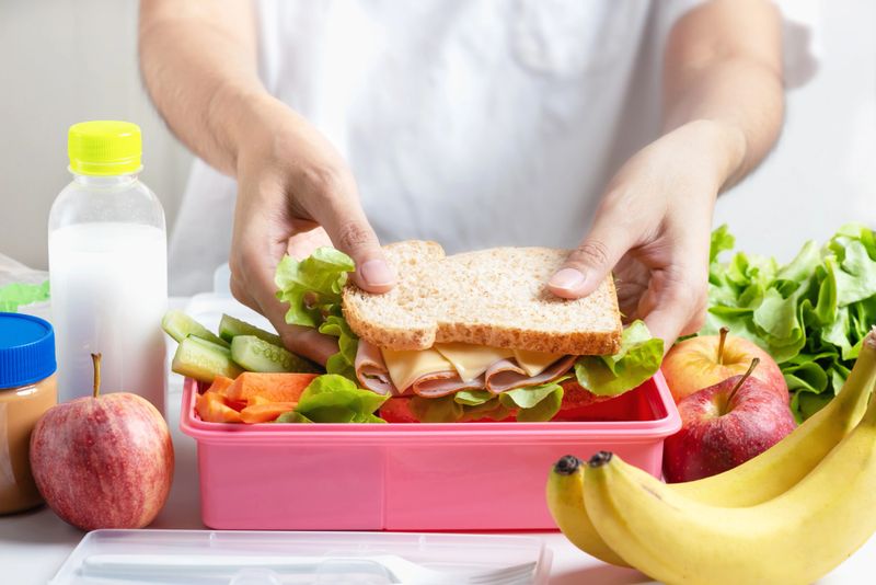 Mother preparing school lunch box set, Ham cheese sandwich with cucumber, carrot and nuts, fruits and vegetable in box. Healthy and Diet food.