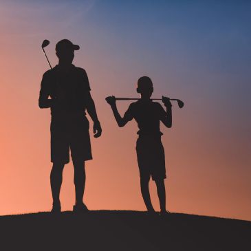 Silhouette of two people holding golf clubs at sunset.