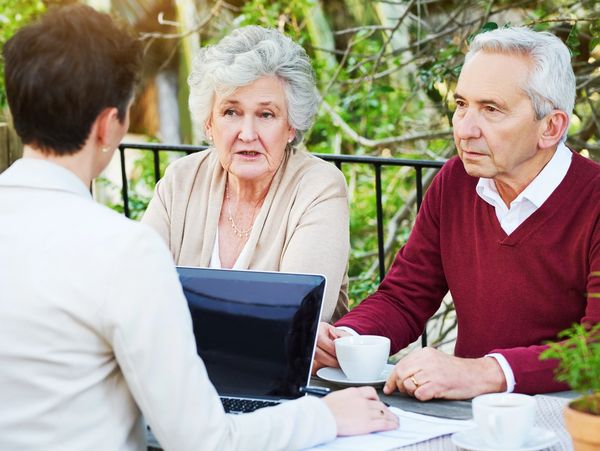 Elderly couple discussing with a professional outdoors at a table.