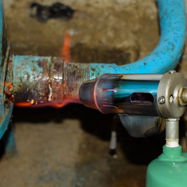 A torch heating a rusty blue pipe fitting.