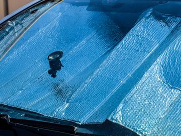 Car windshield covered with a reflective sunshade and a small suction cup device.
