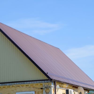 A house with a large brown metal roof under a clear blue sky.