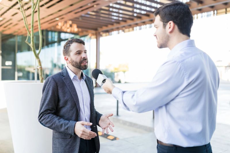 Mid adult famous personality wearing suit and giving interview to broadcaster outdoors