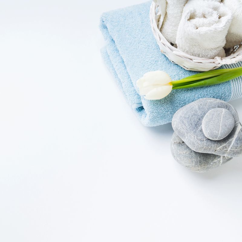 Fresh folded towels, stones and a flower on white background. Spa, bathroom concept