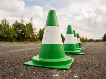 Green and white traffic cones lined up on an asphalt road.