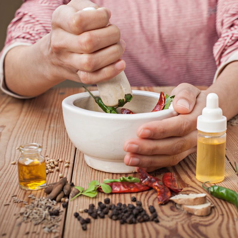 Close-up of woman hands preparing various spices, oil with pestle and mortar on wooden table.