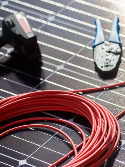Coiled red wire on a solar panel with a crimping tool.
