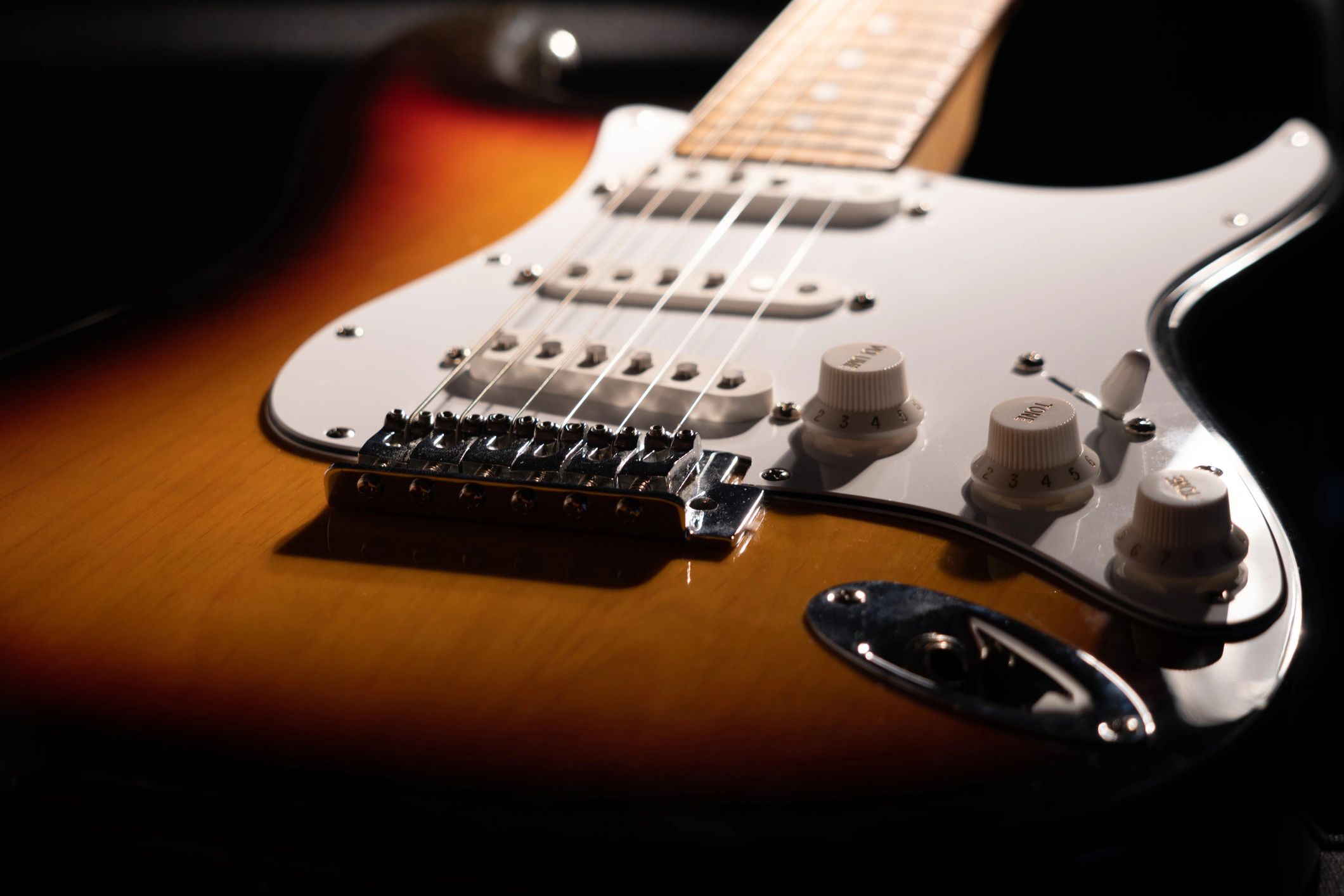 Close-up of a sunburst electric guitar with white pickguard and control knobs.