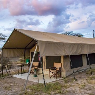 Large beige camping tent set up in a natural area under a cloudy sky.