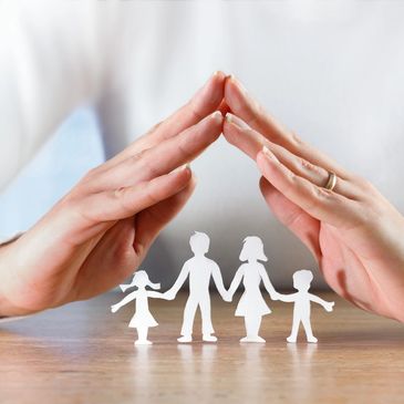 Hands protect paper cutout family on wooden table symbolizing care and security.