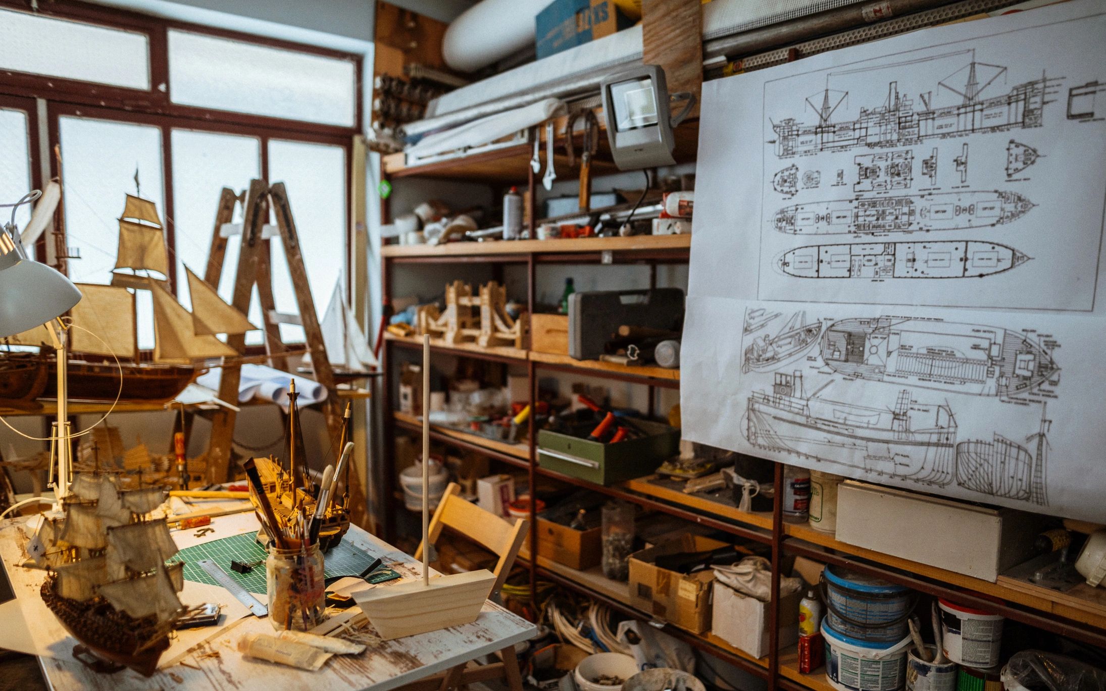 Model shipbuilding workshop with plans and wooden ship models.