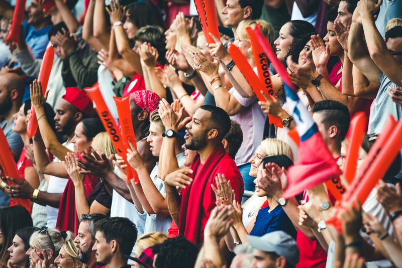 Large crowd in a football stadium cheering for their team with their hands raised and clapping.