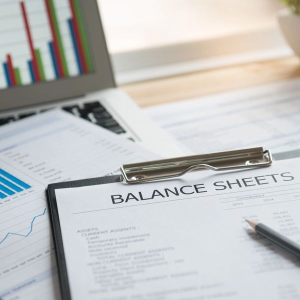 Close-up of financial balance sheets and charts on a desk with a laptop.