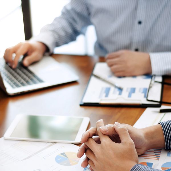 Two professionals working on financial reports and charts with a laptop and tablet.