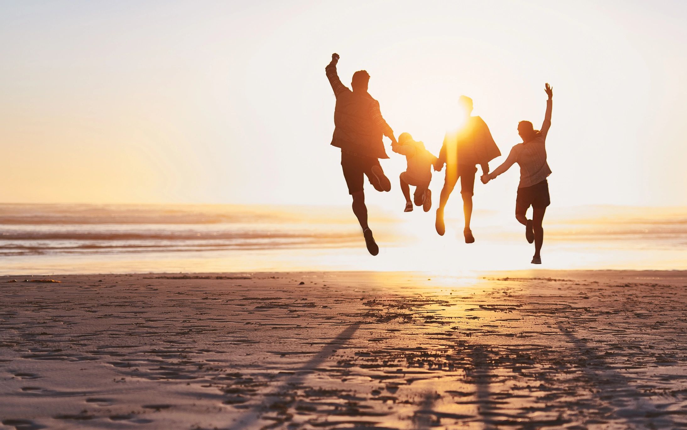 Four people jumping joyfully on the beach at sunset.