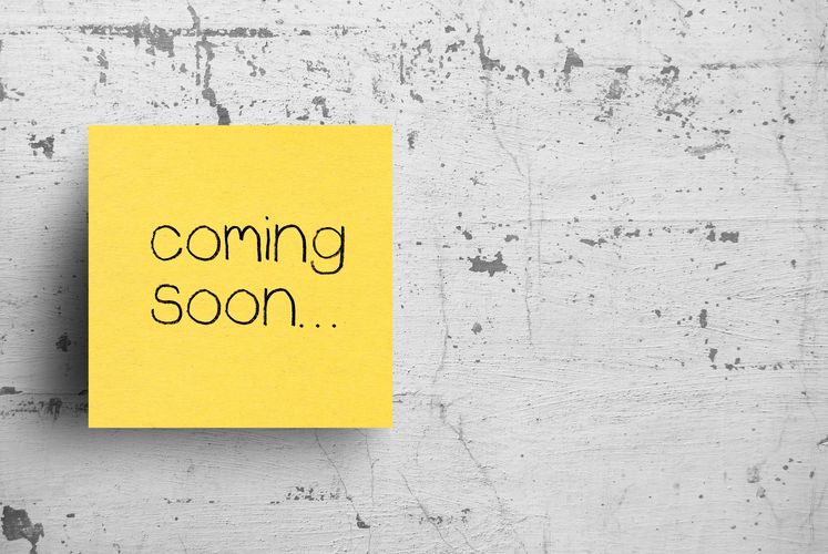 Yellow sticky note with 'coming soon...' on a textured gray wall.
