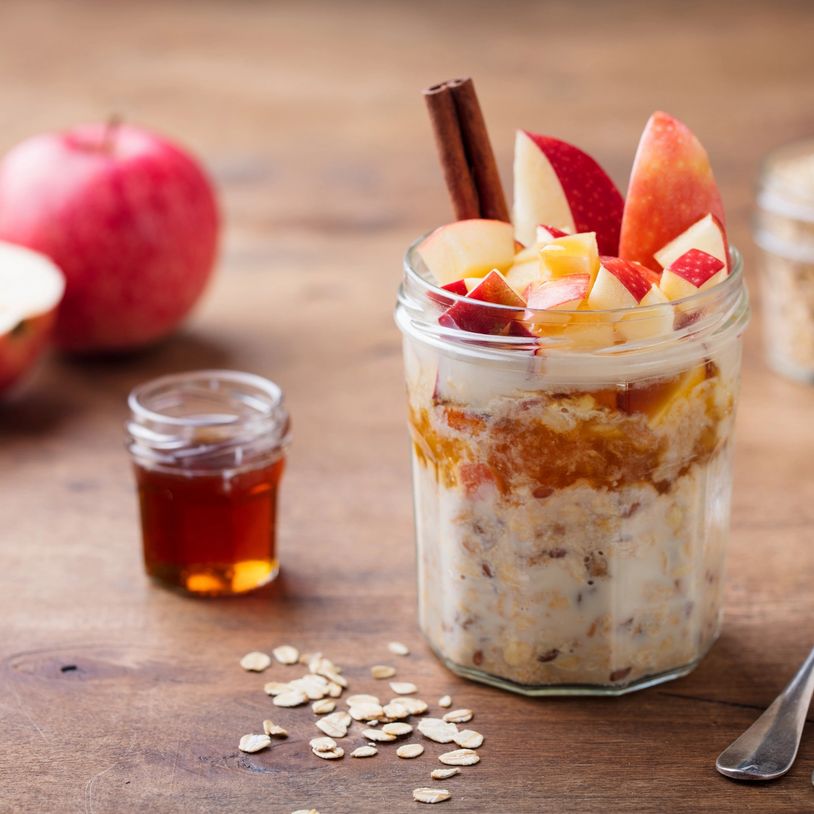 Overnight oats topped with fresh apple slices and cinnamon sticks in a glass jar.