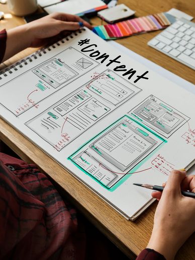 Person sketching website content layouts in a notebook.