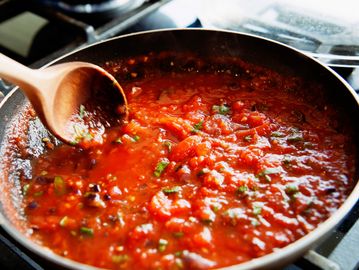 A pan of tomato sauce being stirred with a wooden spoon.