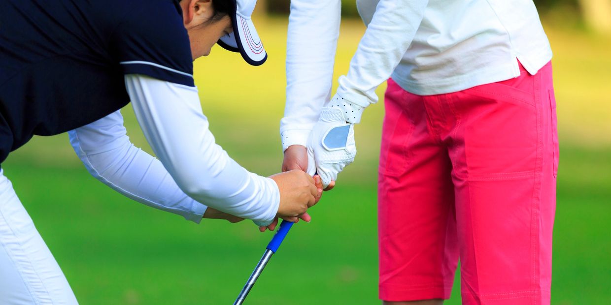 A golf instructor teaching a player how to hold a golf club.