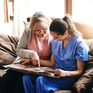 Elderly woman and nurse looking at a photo album together on a couch.