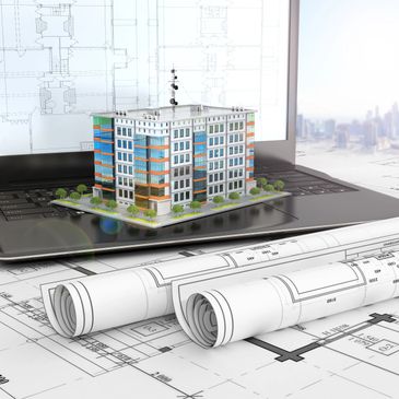Architectural model of a building on a laptop with blueprints.