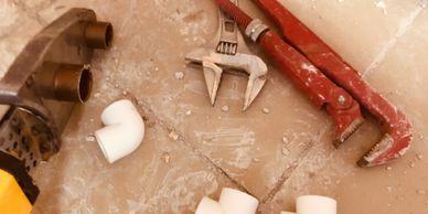 Plumbing tools and pipe fittings on a tiled floor.