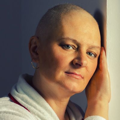 Portrait of a contemplative woman with a shaved head leaning against a wall.