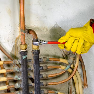A worker in yellow gloves tightening a pipe fitting with a wrench.