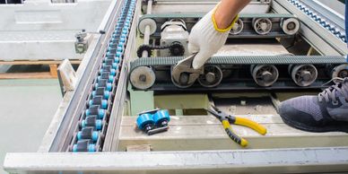 A person repairing a conveyor belt with tools and gloves.