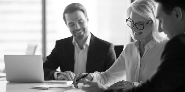 A group of persons in professional clothing smiling around a table while reviewing legal documents.