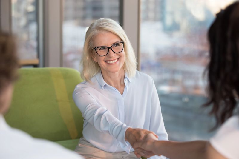 Smiling confident old mature woman job seeker applicant handshaking hr making good first impression at interview meeting, happy satisfied middle aged businesswoman shaking hand getting hired concept