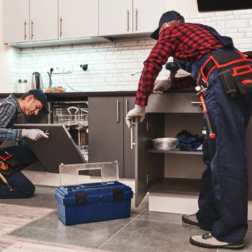 Two repairmen fixing kitchen cabinets and dishwasher with tools.
