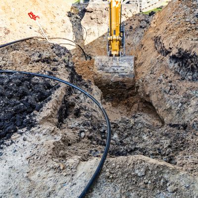 Excavator digging a trench with black cables laid out.